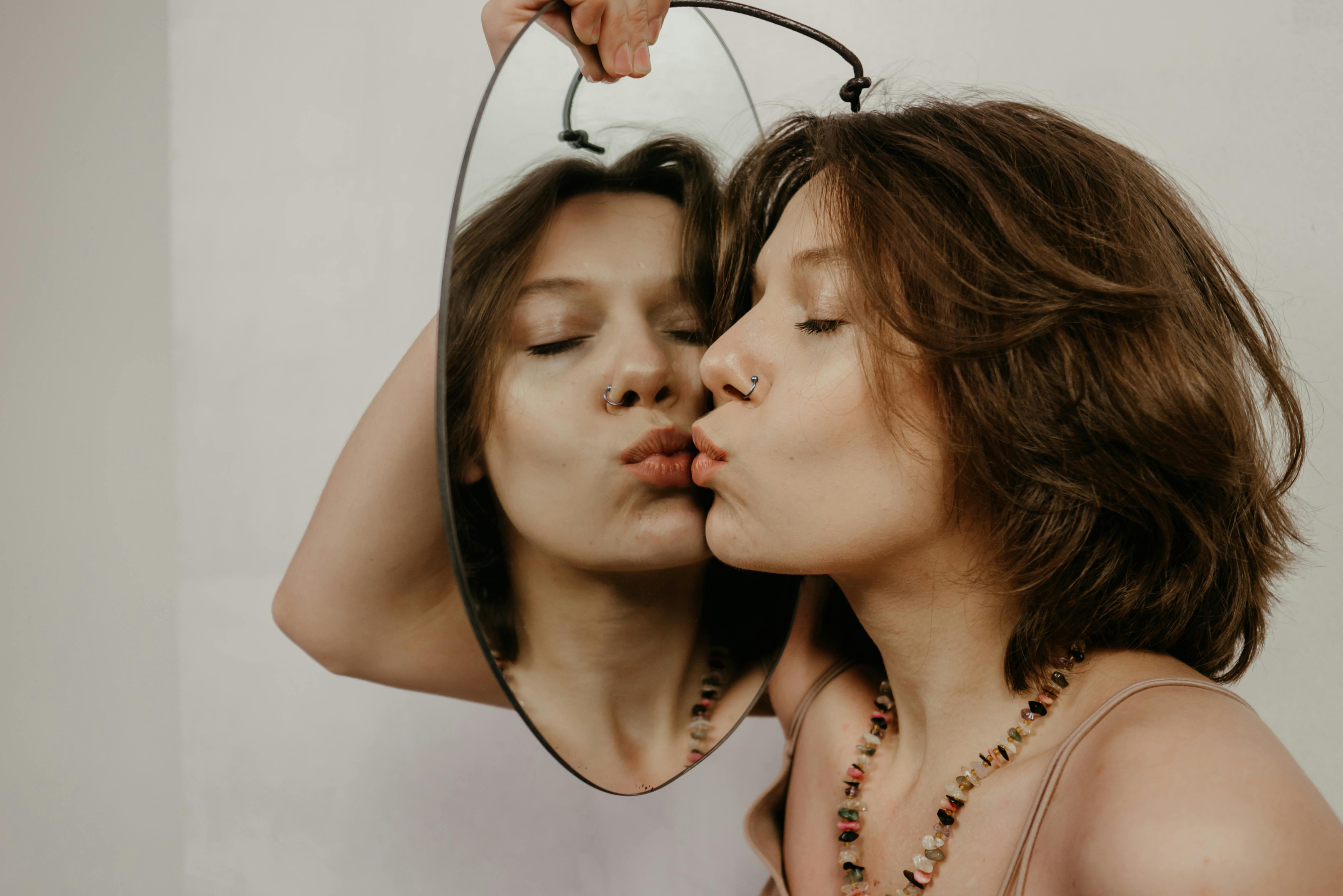 Woman tenderly kissing her reflection in a mirror, symbolizing self-love and acceptance.